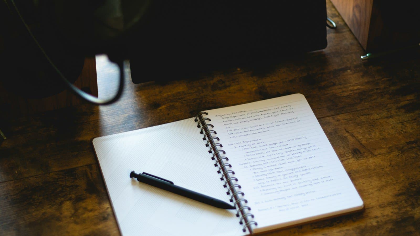 A notebook and pen on a wooden desk, photographed by Gabriel Cox.